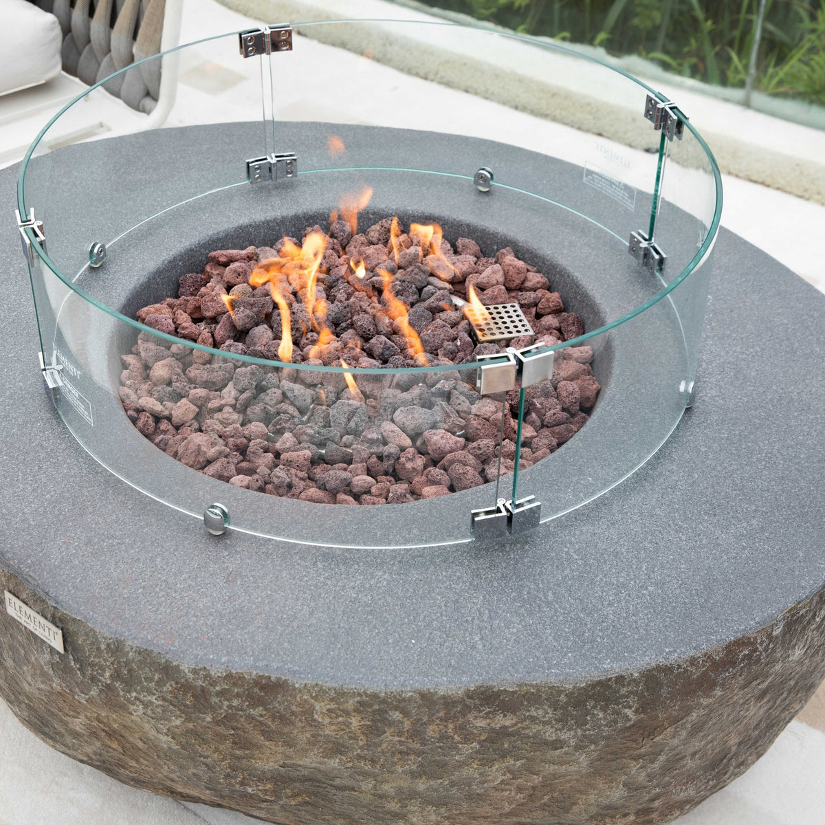 Elementi Boulder Fire Pit - Curved Tempered Glass Windscreen Installed with Active Flame on Patio
