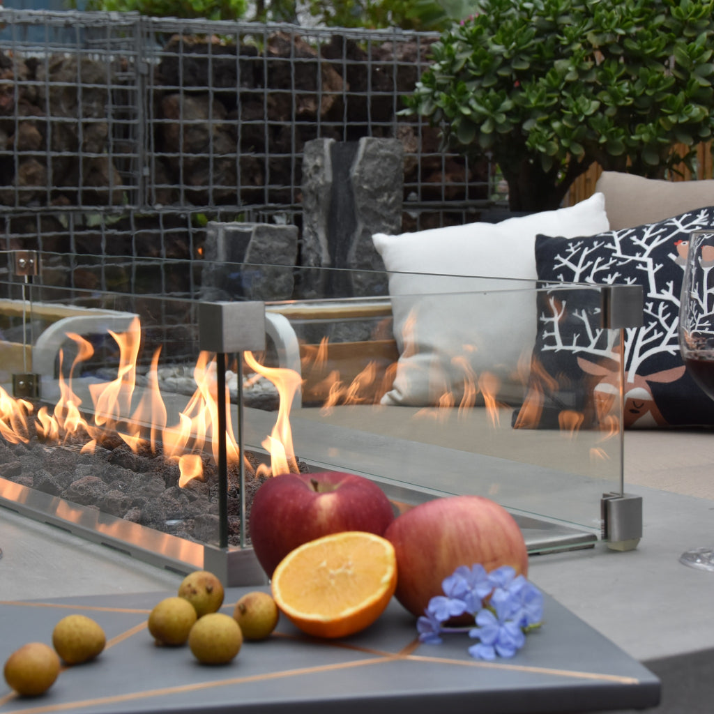 Elementi Granville Fire Table Light Gray - Glass Windscreen and Vibrant Flame with Wine Glasses on Evening Patio