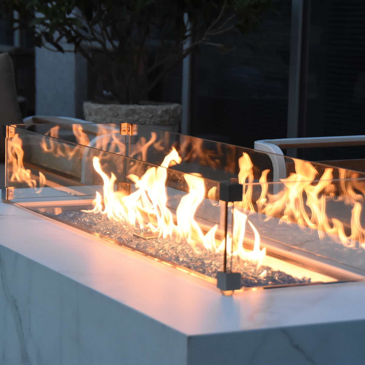 Elementi Plus Carrara Fire Table - Dusk Patio Setting with Glass Windscreen and Glowing Fire